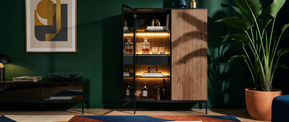 Modern interior with an illuminated Lampy display cabinet against a dark green wall, with plants and decorations