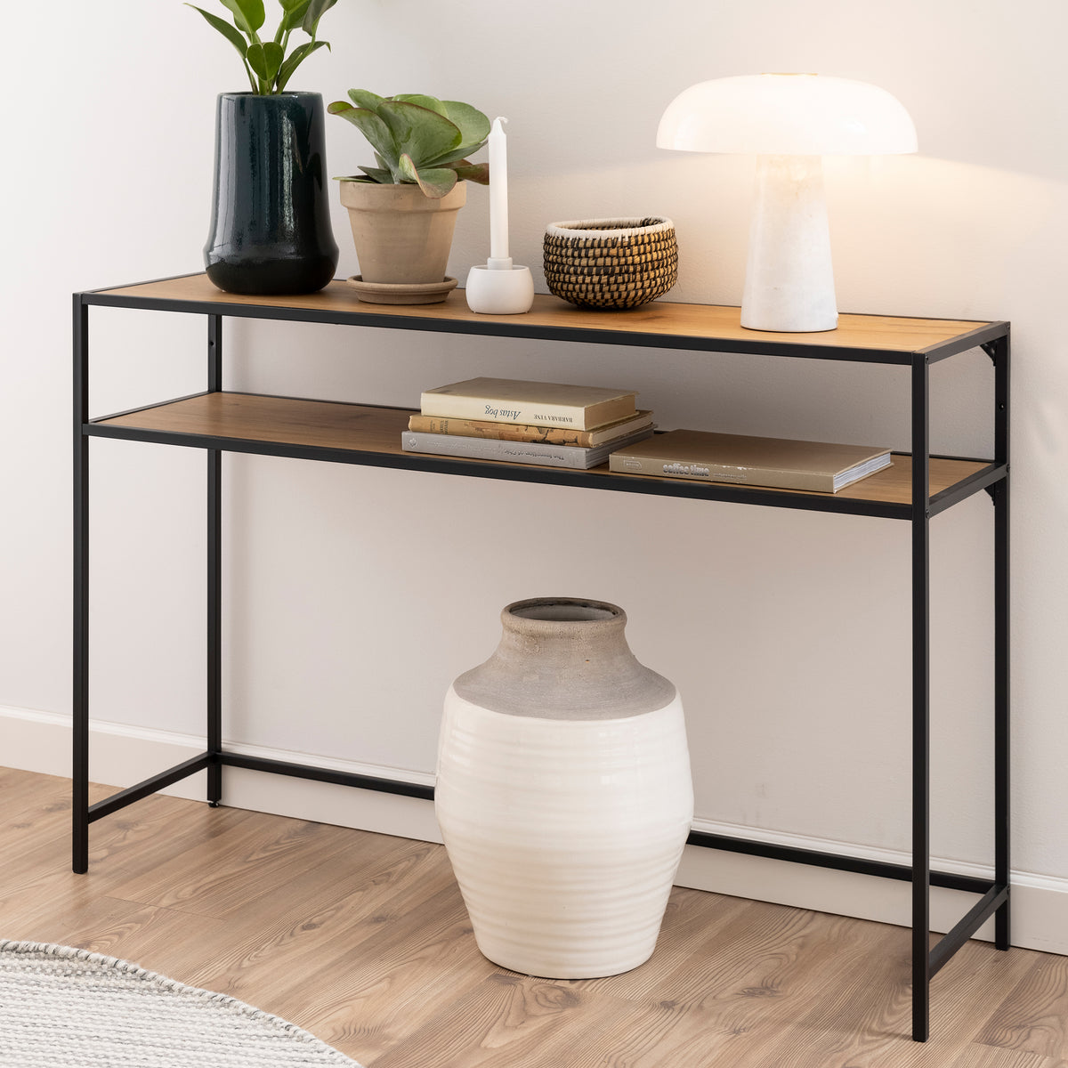 Skeleto-consoletafel 120x79 in de kleur ‘Wild Eiken’ tegen een lichte muur, met een lamp, planten en boeken op de plank – een consoletafel voor de hal