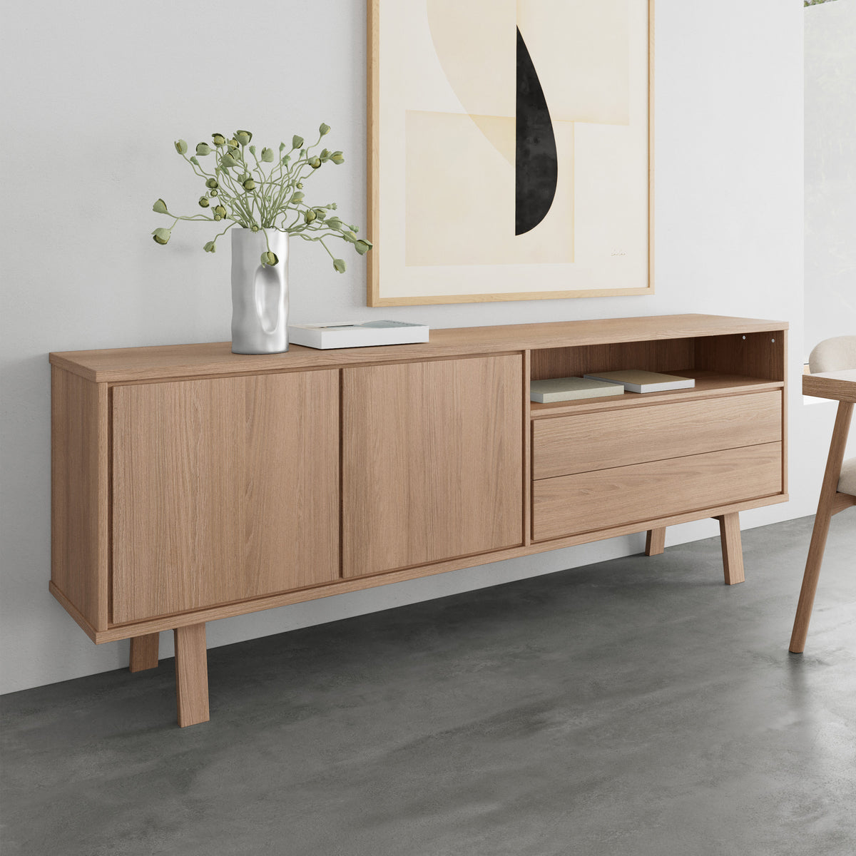 Lurisse-commode 200x75, gebleekt eikenhout, onder de afbeelding tegen een grijze muur, met een vaas en boeken – een commode voor de woonkamer