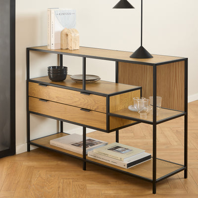 Laag Skeleto-rek 114x78 in de kleur ‘Wild Eiken’ onder een zwarte lamp, met boeken, kommen en glazen op de planken