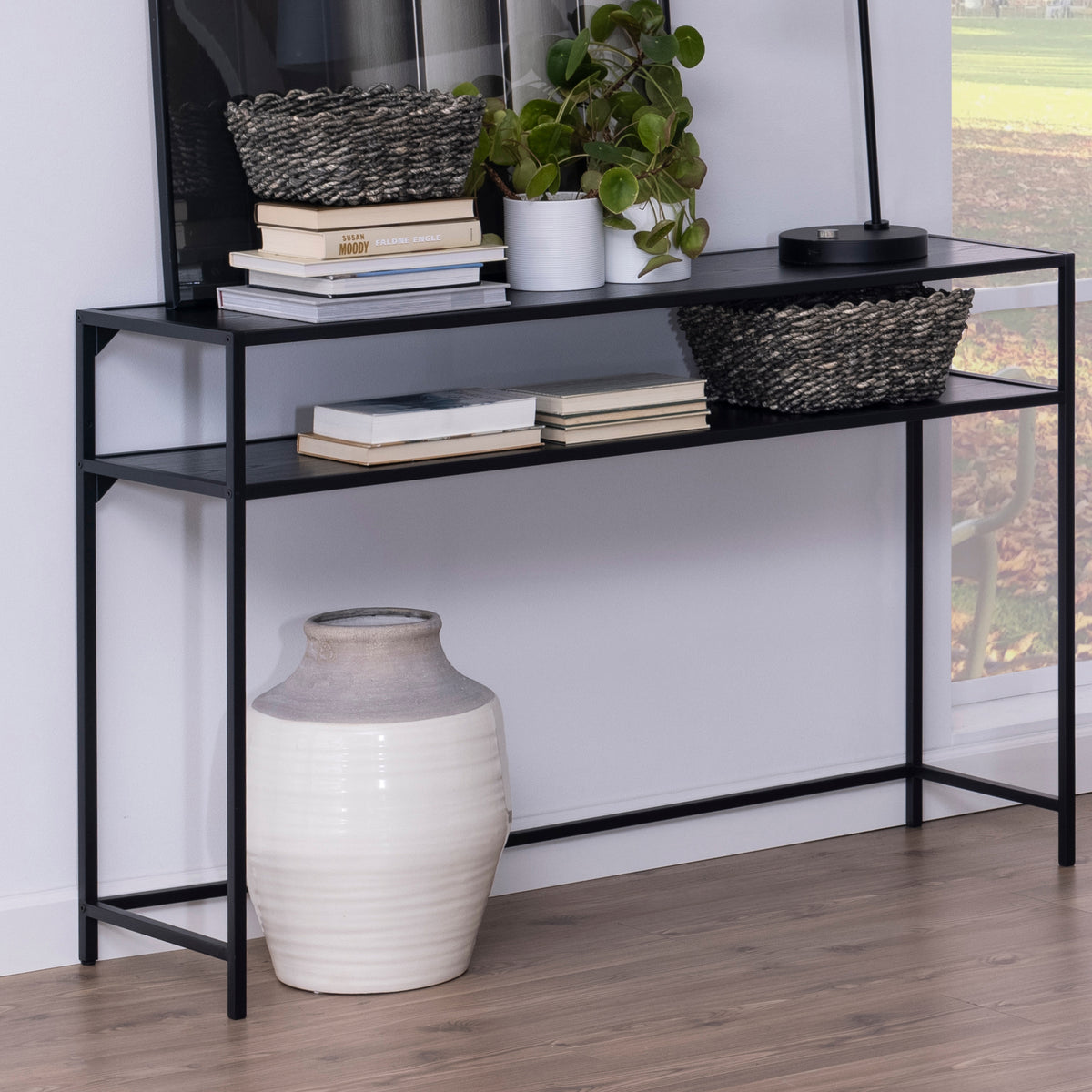 Skeleto-consoletafel 120x79, zwart melamine, tegen de muur geplaatst met manden, boeken en een plant, met een vaas eronder