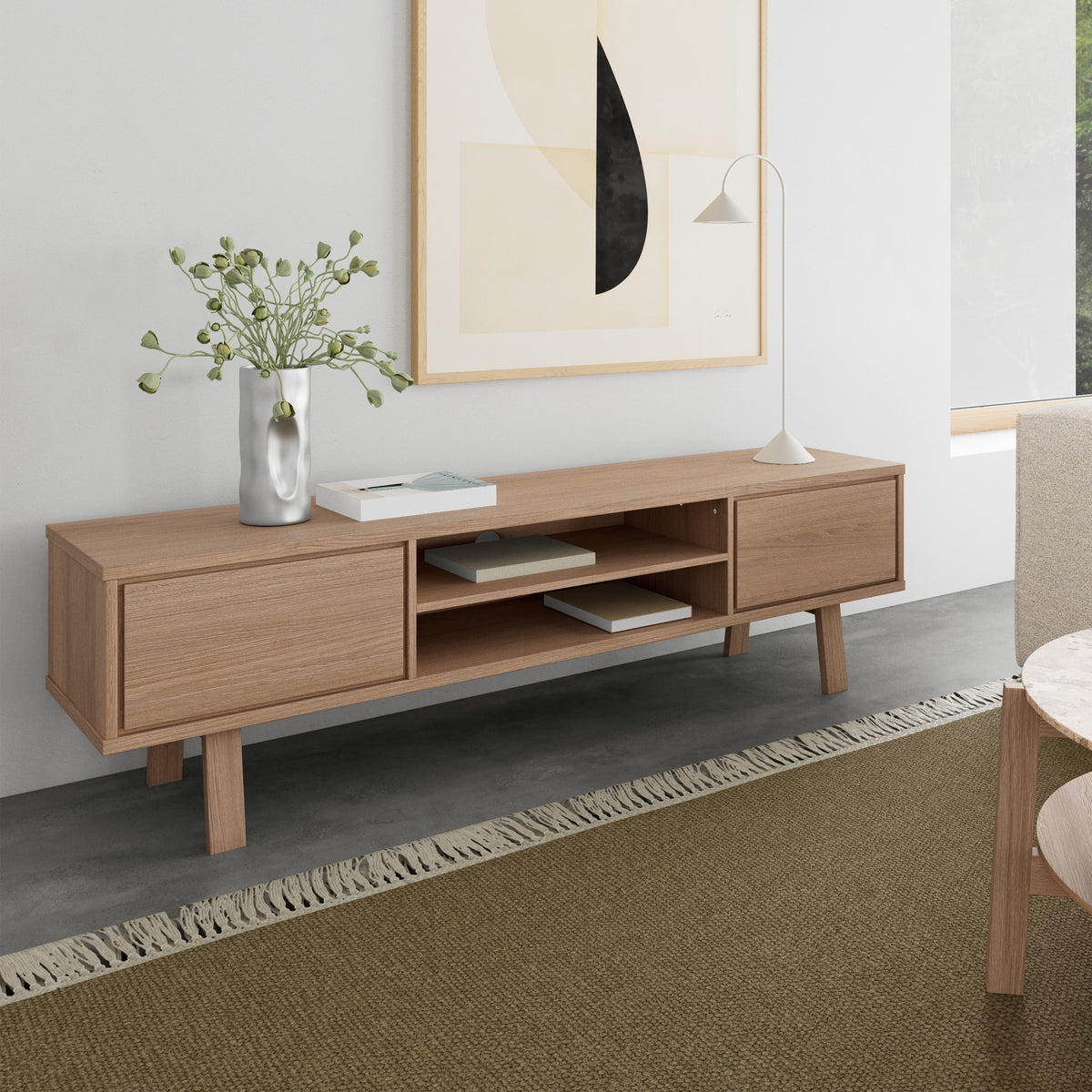 Lurisse TV-kast 180x50, gebleekt eiken, in de woonkamer onder een kunstwerk, met een lamp, een vaas en boeken op een olijfgroen tapijt