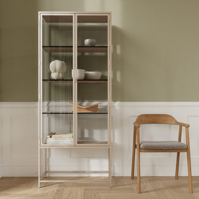 Vitrine Skeleto 77x186 grijze melamine tegen een olijfgroene muur naast een houten stoel – een vitrine voor keramiek en boeken